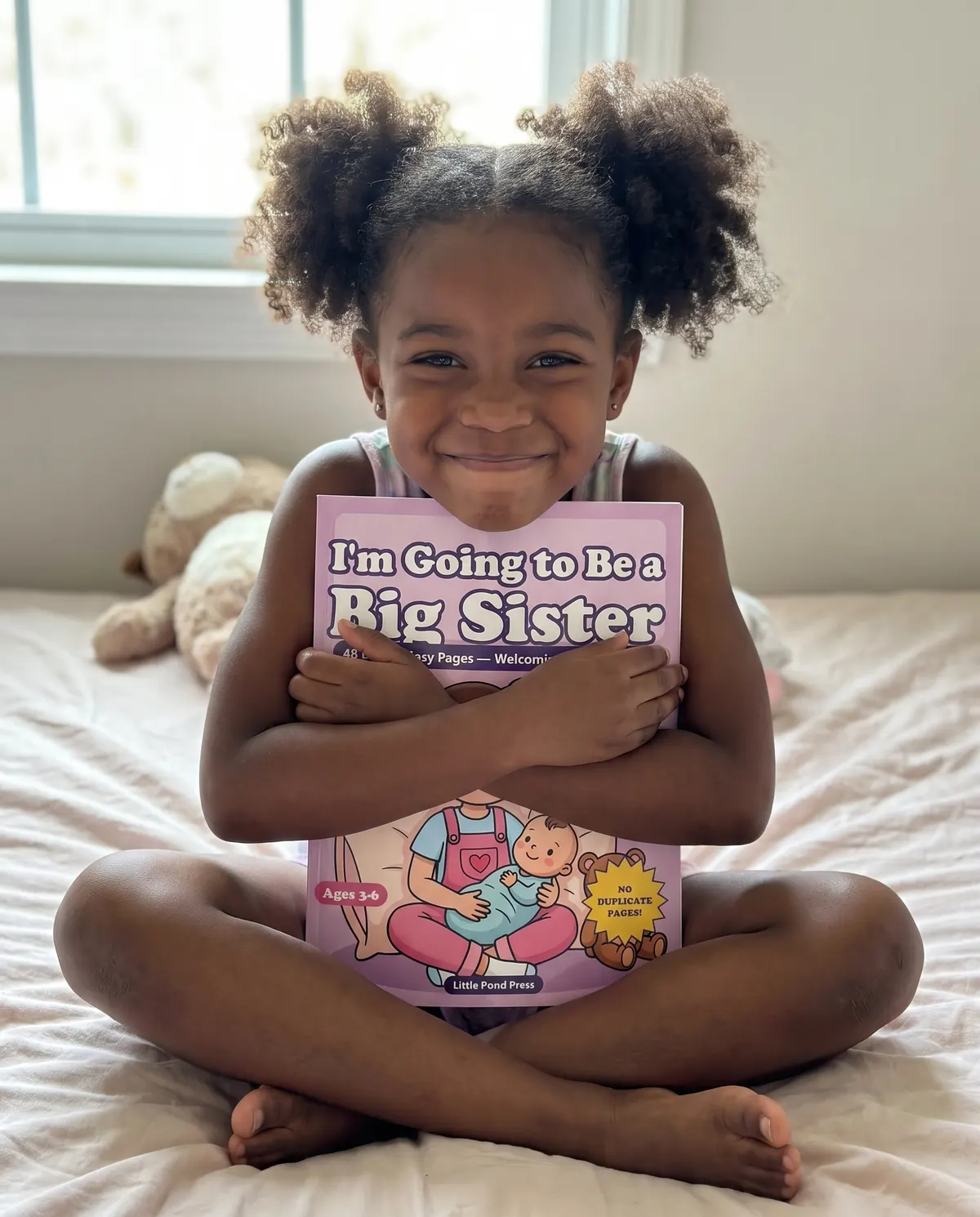 A girl sitting cross-legged on a bed hugging the Big Sister coloring book