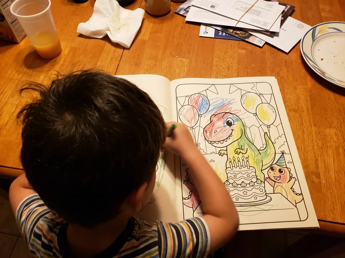 A boy at a kitchen table coloring a dinosaur page